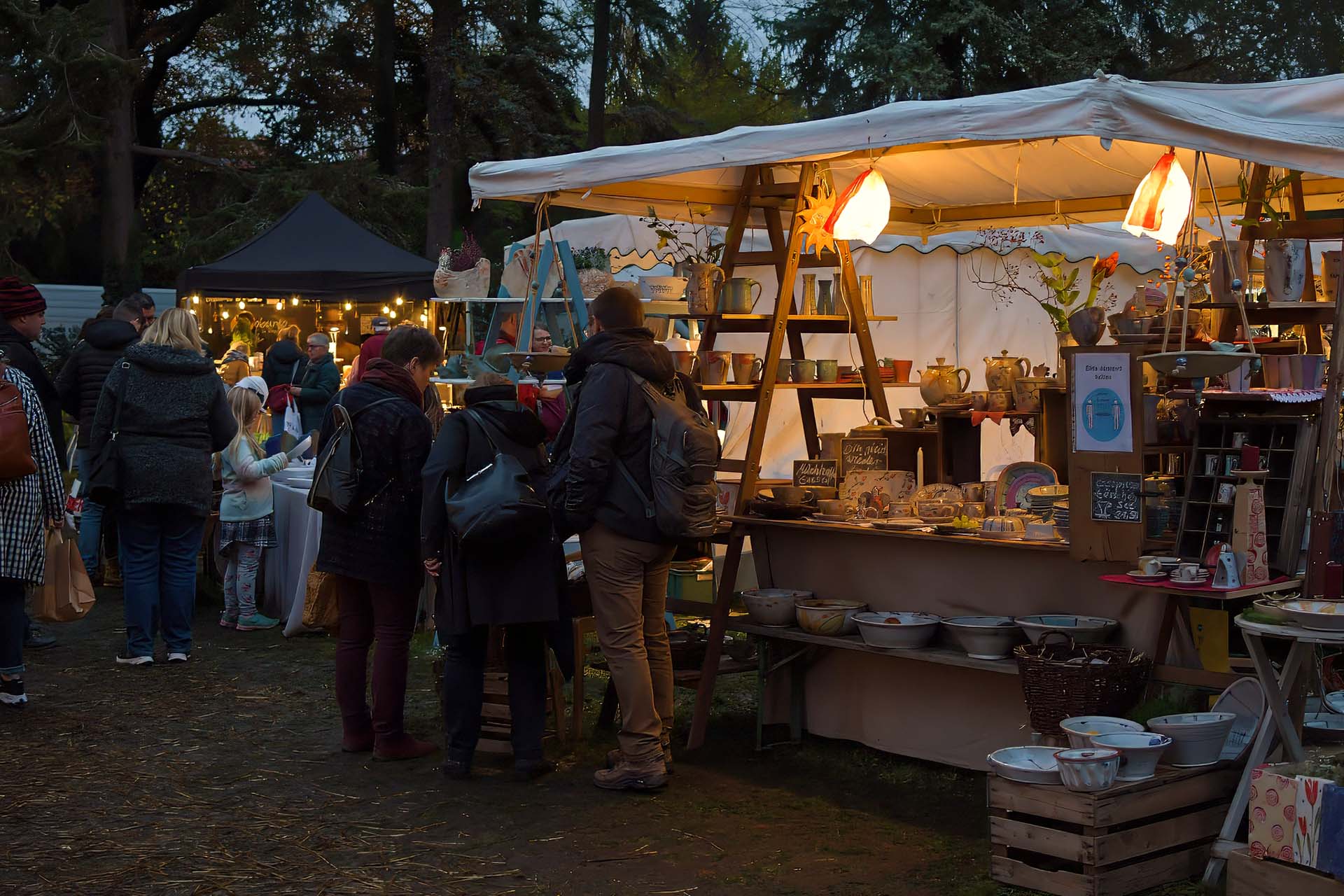 Besucher an einem Keramikstand mit leuchtender Sternenlaterne am Abend.