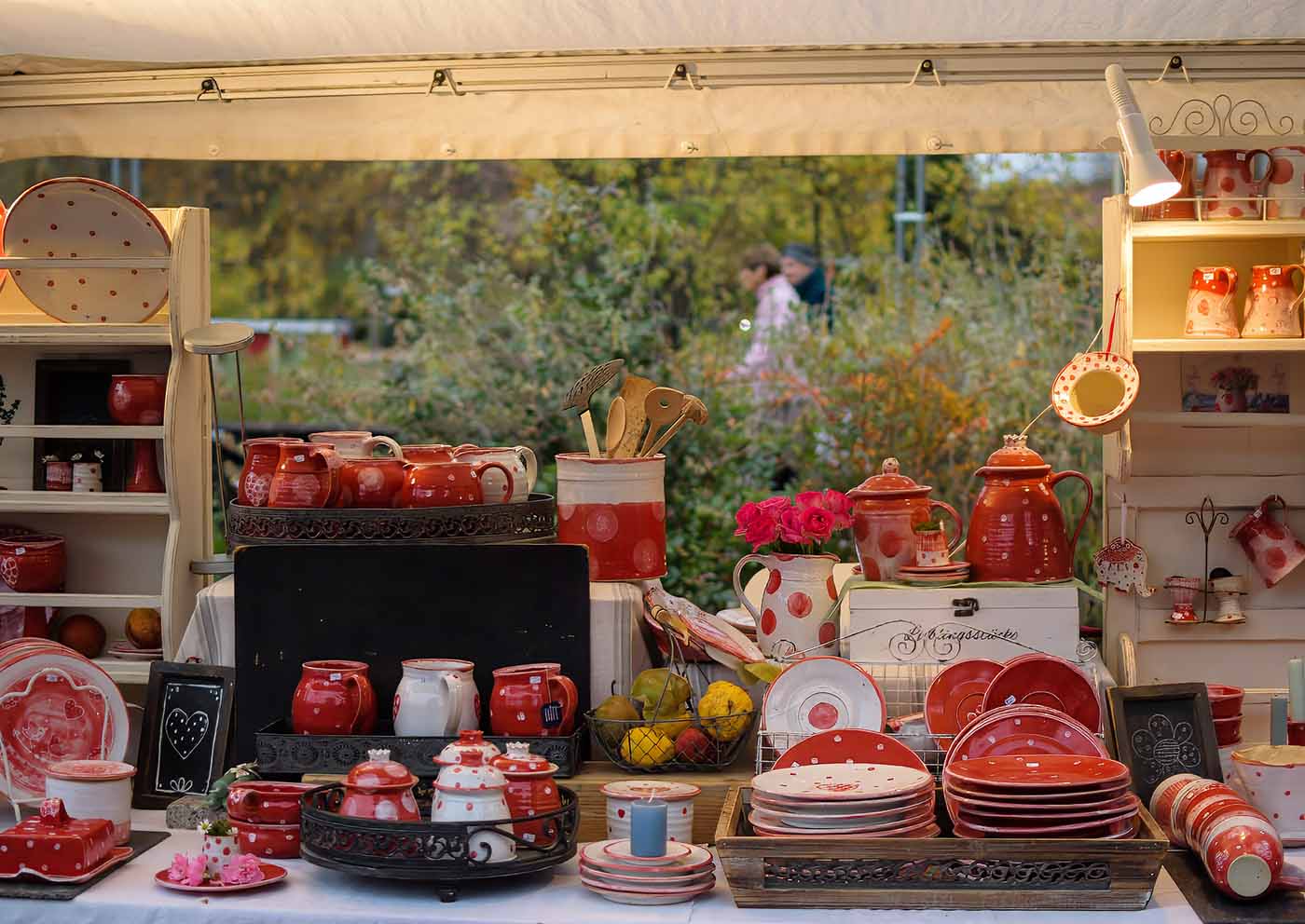 Marktstand mit rot glasierter Punkte-Keramik – Teller, Krüge und Schalen im goldenen Abendlicht.